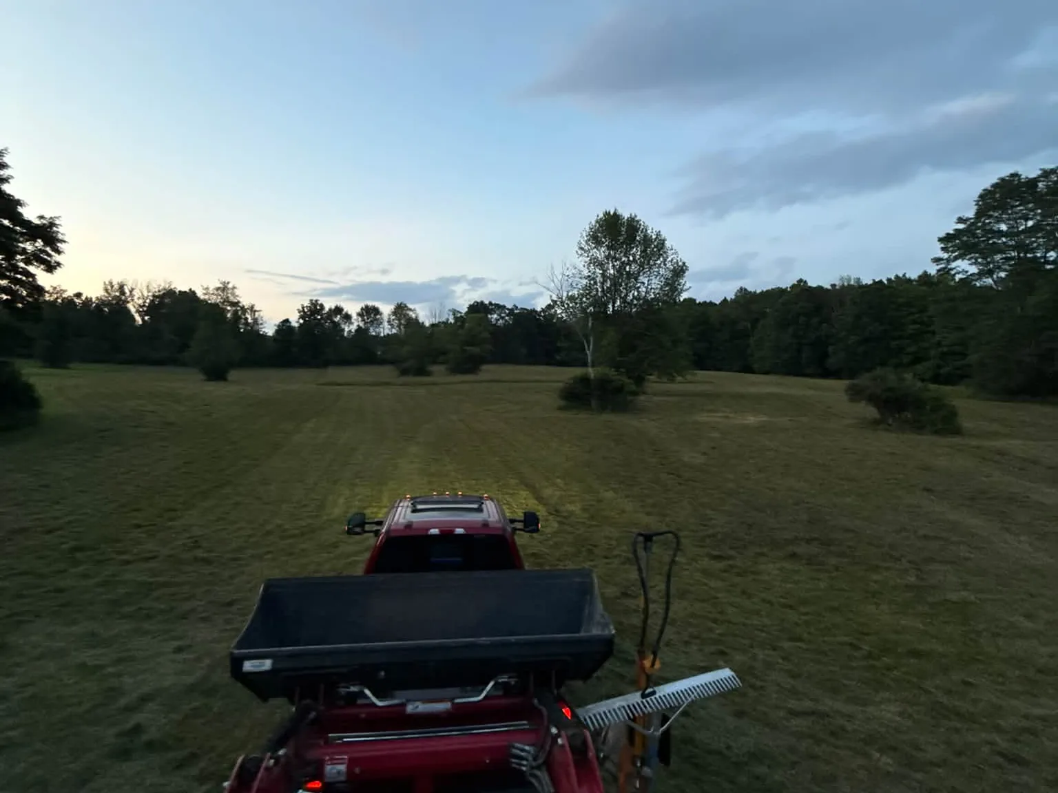 Brush hogging an open pasture at dusk from the tractor, field cut short