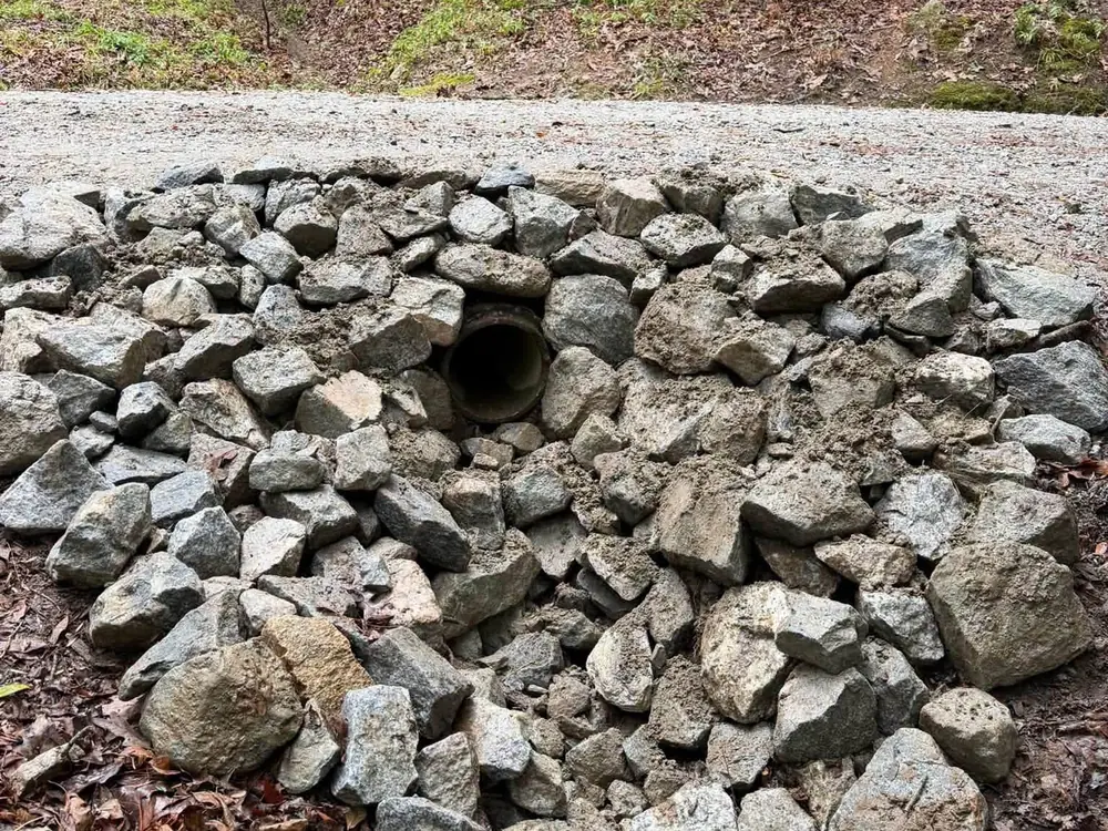 Culvert pipe set in a stone lined outlet beside a gravel drive, drainage work for french drain and culvert jobs