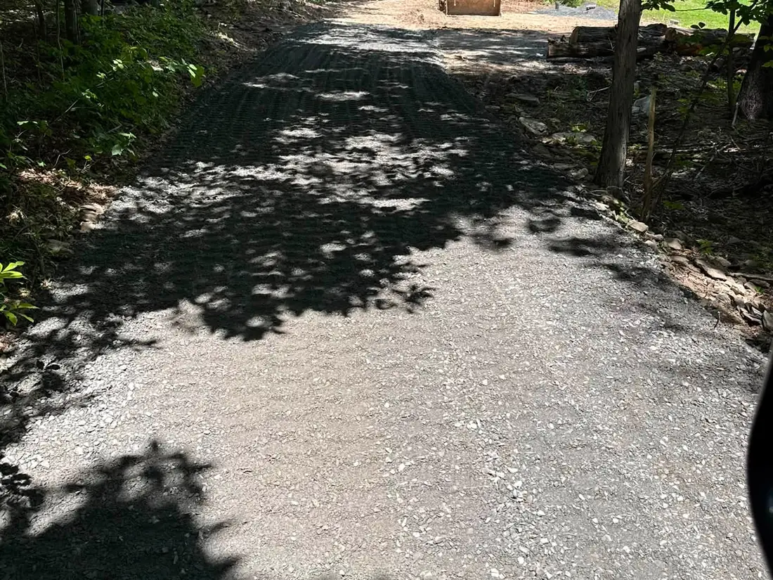 Gravel driveway installation through shady woods, stone spread and leveled to the work area