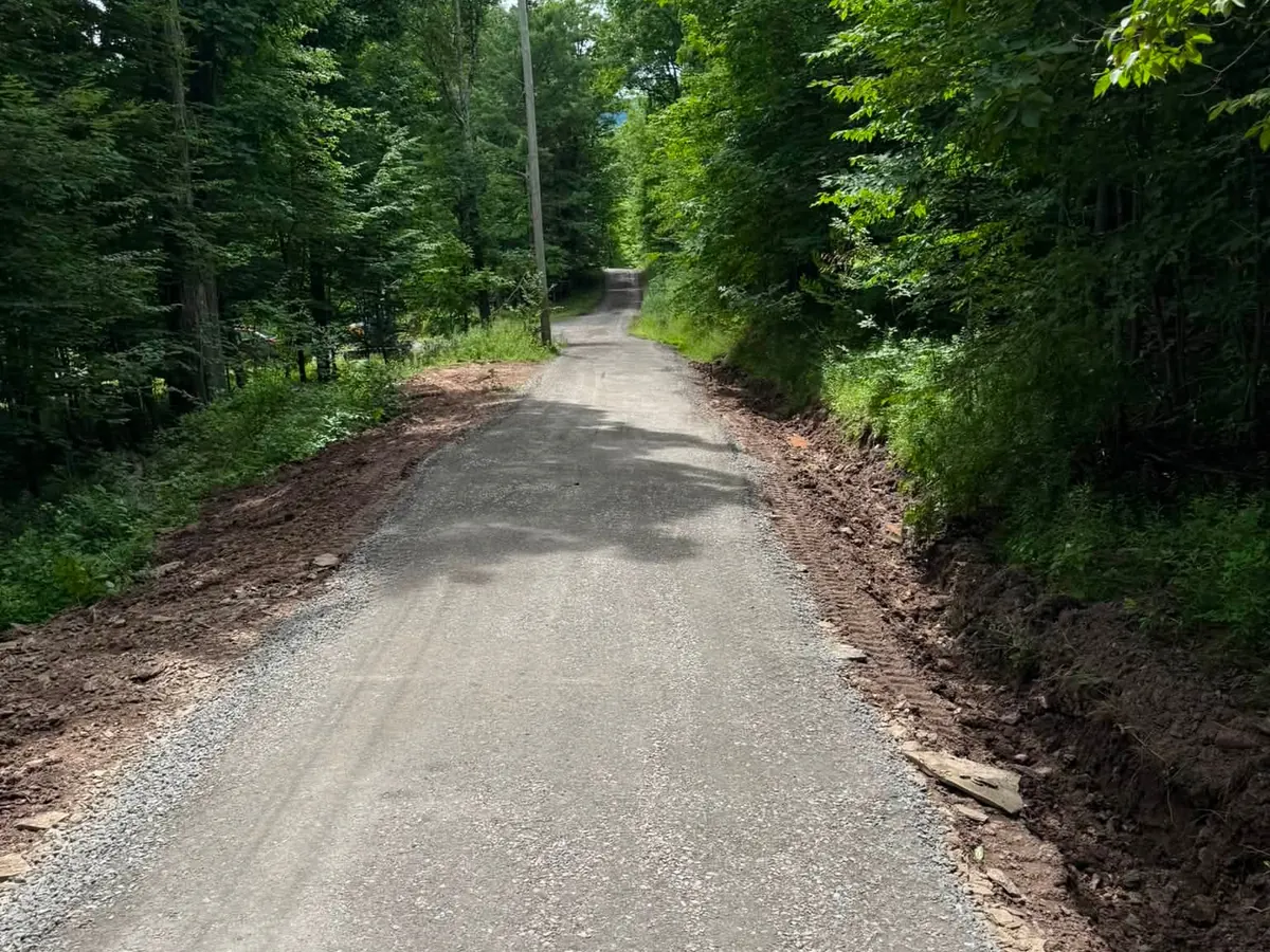 Gravel driveways: a driveway rebuilt with fresh stone through the woods, cleaned up shoulders on both sides