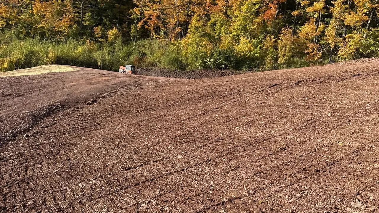 Excavation contractor grading a large hillside site of red shale soil below fall woods