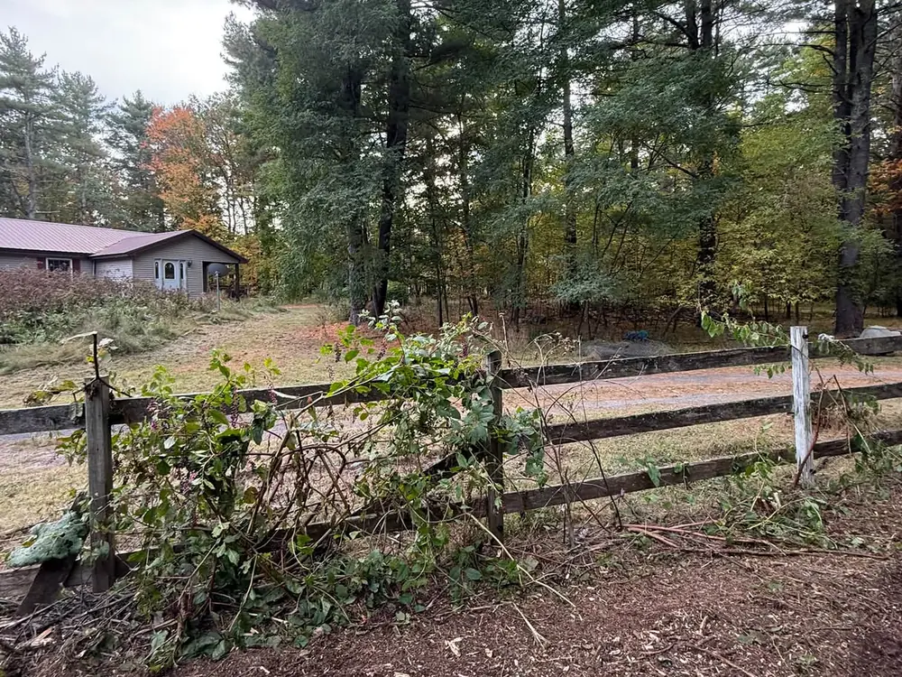 Fence line brush being cleared on a farm property with red barns behind, land clearing