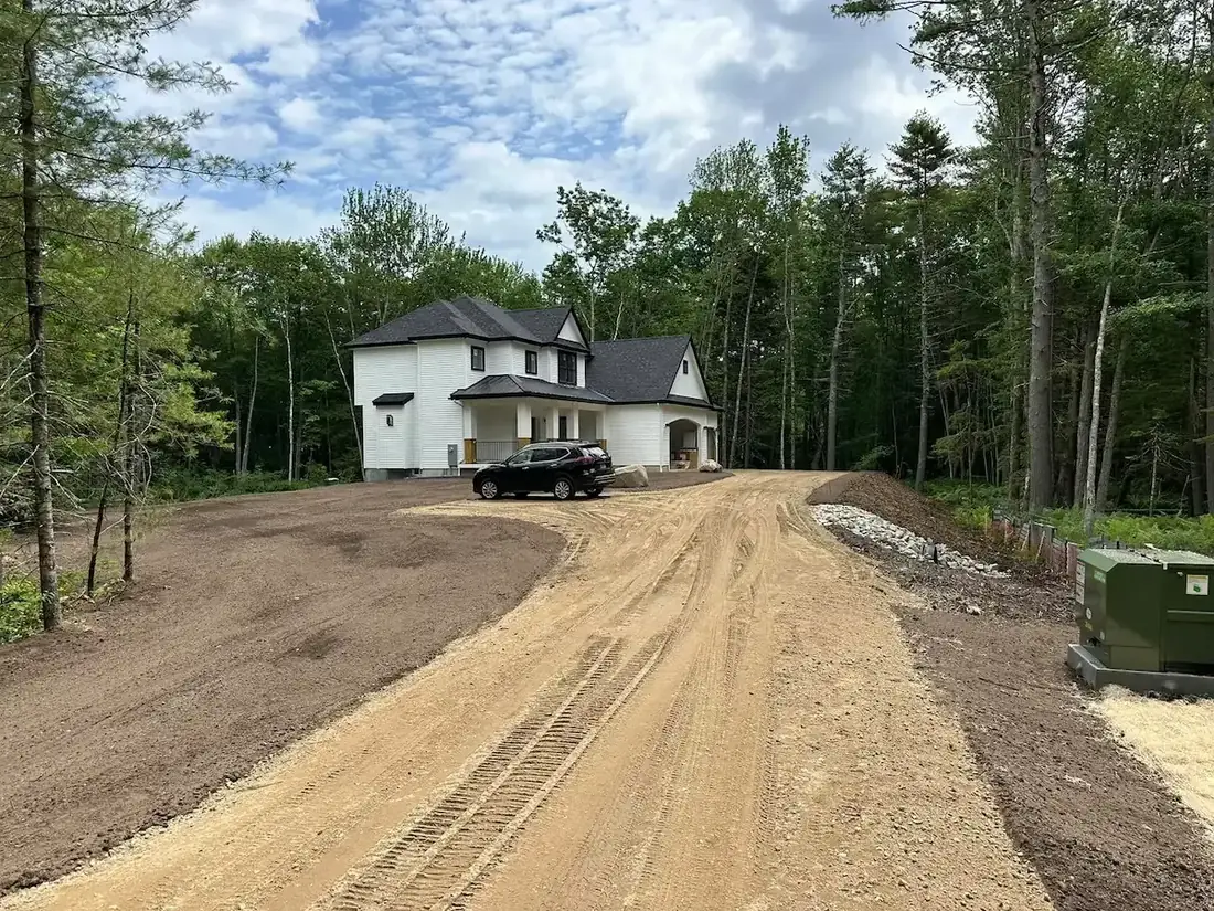 Finish graded topsoil on both sides of a new gravel drive at a house on a wooded lot, land grading
