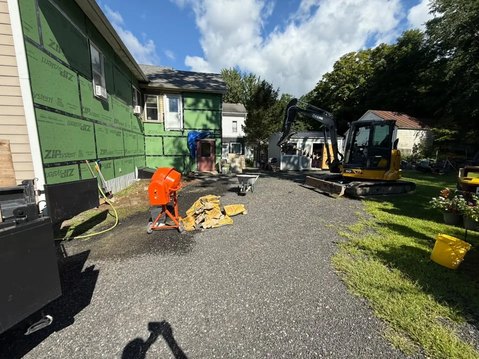 Mini excavator working on a gravel drive beside a house, septic system installation