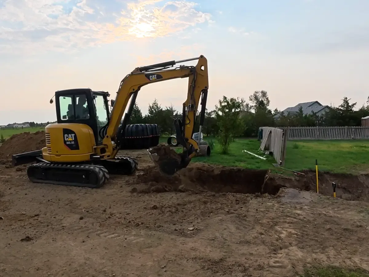Mini excavator digging a septic tank hole in a back yard, tanks waiting on the grass, septic system installation