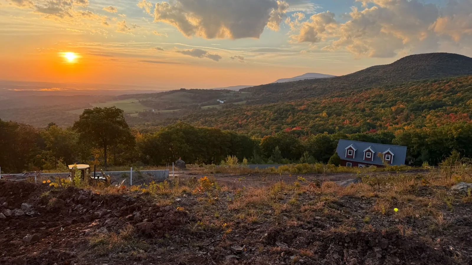 Sunset over wooded mountains from a hilltop job site with fresh dirt work in front